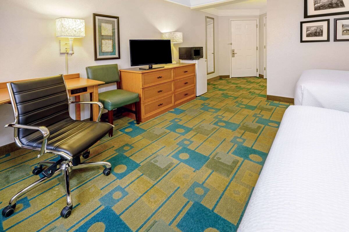 Quarto de hotel com cama, escrivaninha, cadeira, televisão, micro-ondas e cômoda.