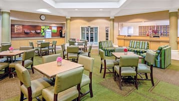 Un hall de hotel con varias zonas de estar, que incluyen mesas y sillas, y un mostrador de recepción.