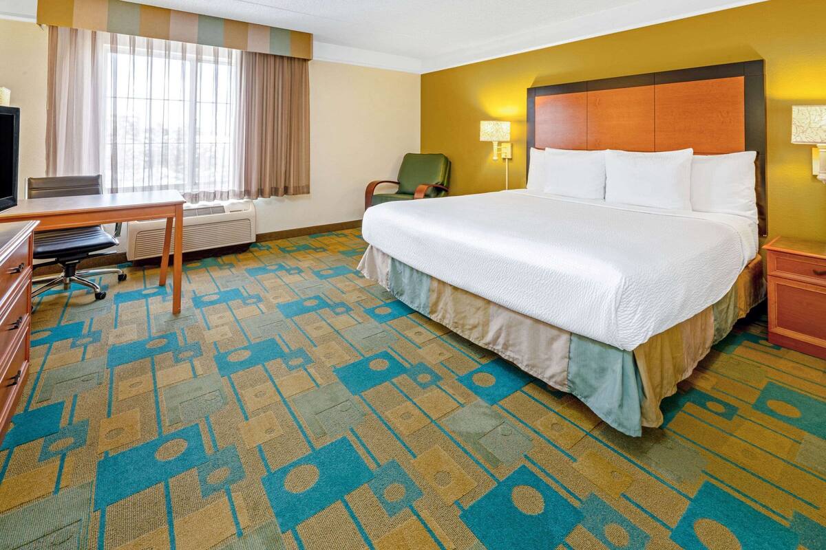 Quarto de hotel com uma cama grande, uma escrivaninha com cadeira, televisão e janela com cortinas.