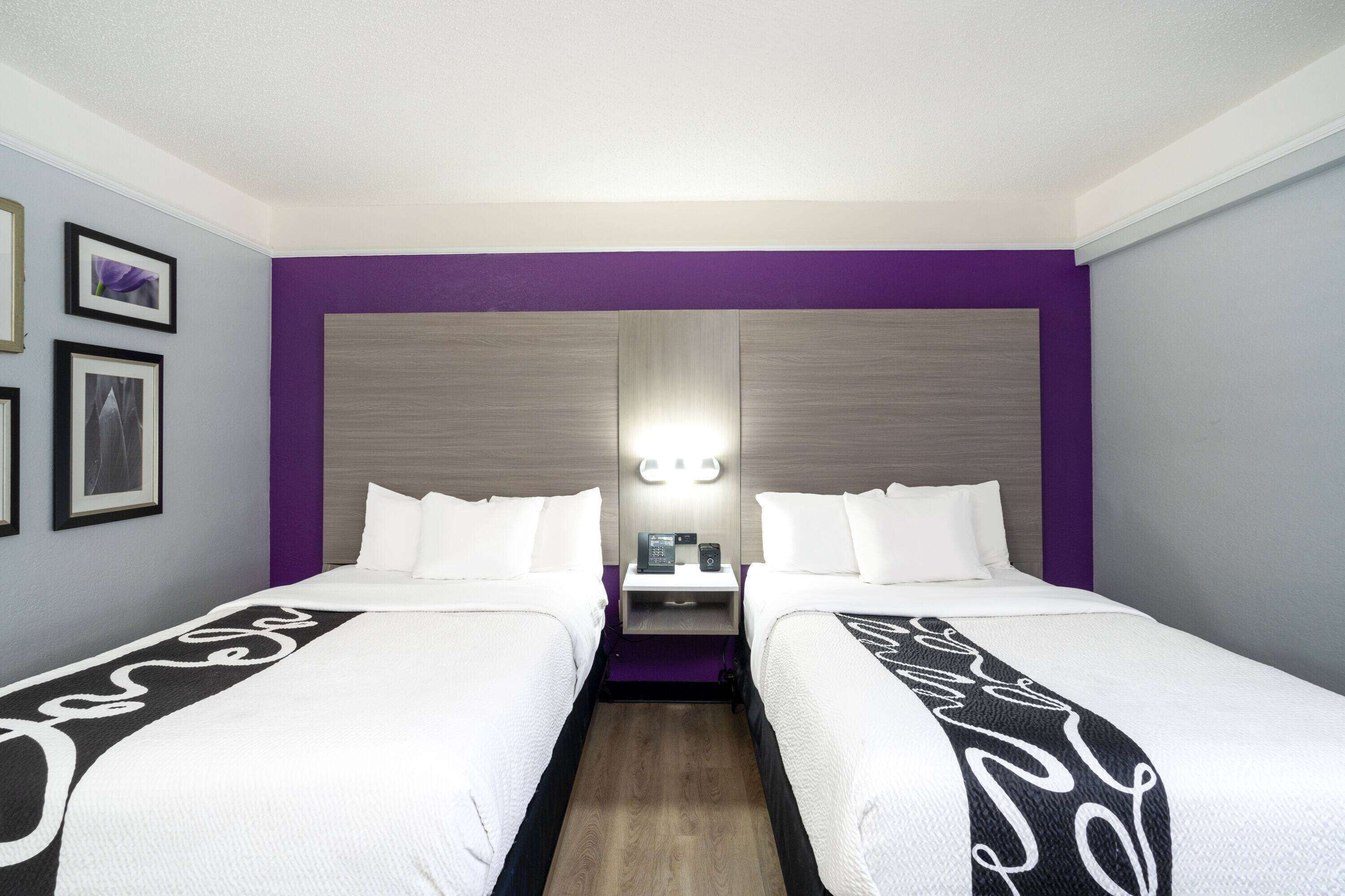 A hotel room with two beds, a nightstand, a lamp, and framed pictures on the wall.