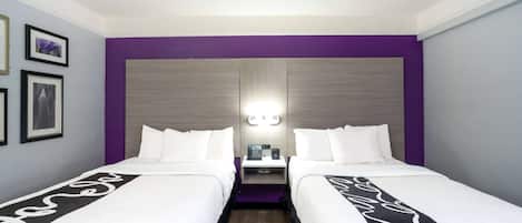 A hotel room with two beds, a nightstand, a lamp, and framed pictures on the wall.