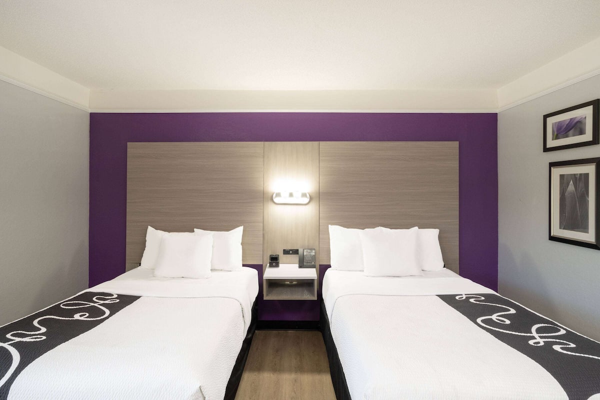 Habitación de hotel con dos camas, una mesita de noche y una lámpara de pared.