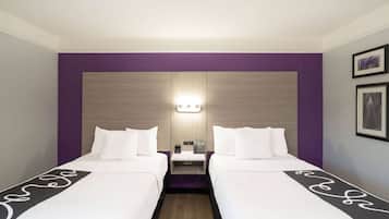 A hotel room with two beds, a nightstand, and a wall-mounted light.