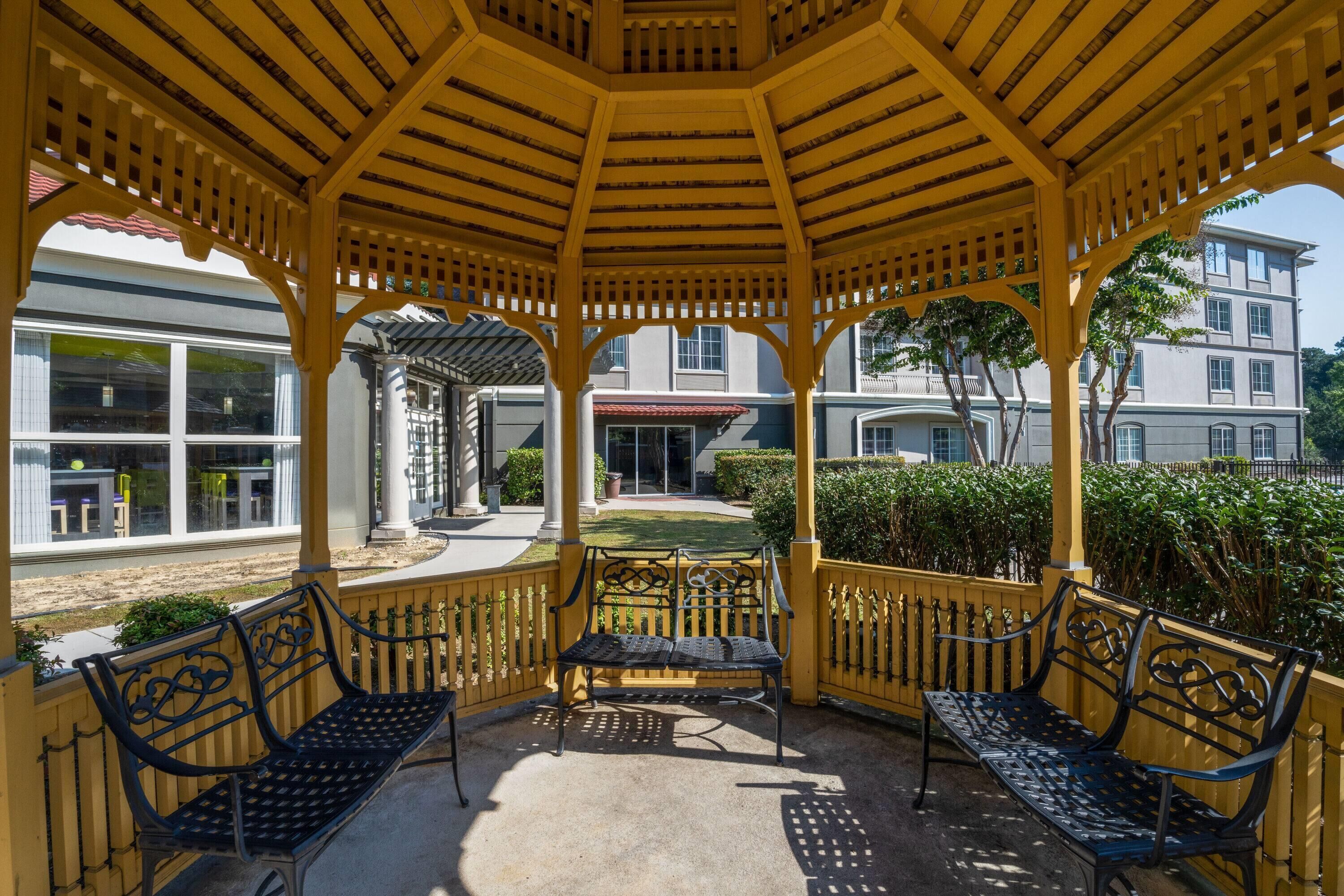 Uma área de estar coberta ao ar livre, com duas bancos e uma estrutura de pérgola.
