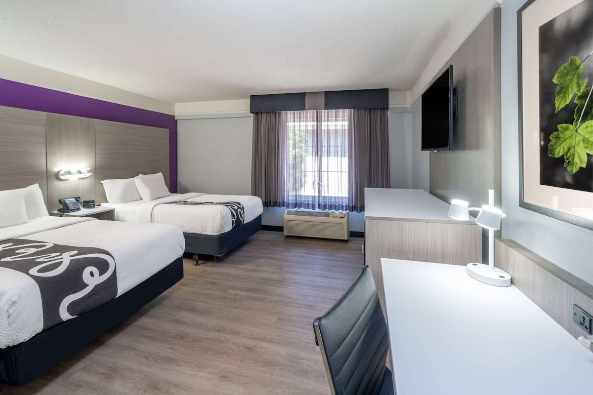 Habitación de hotel con dos camas, un escritorio, una silla, un televisor y una ventana con cortinas.