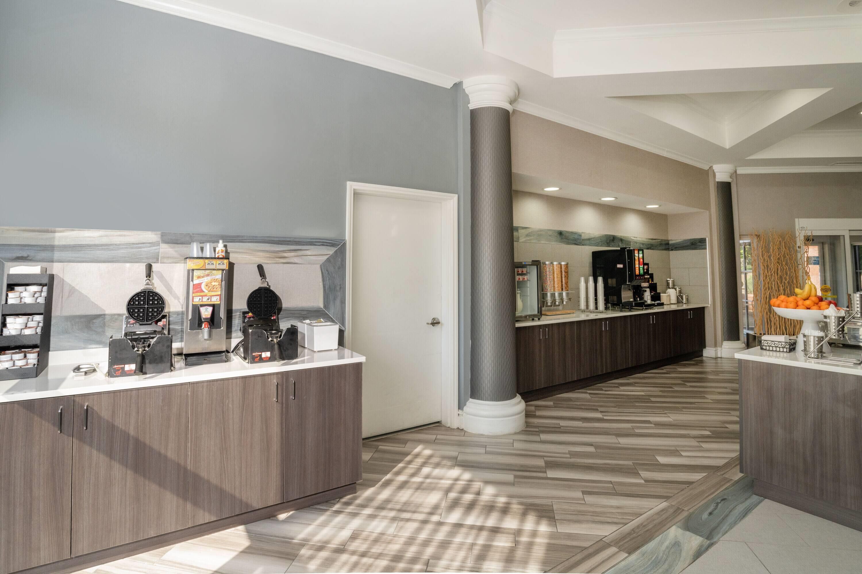 A modern hotel lobby with a self-service breakfast area, a large column, and a check-in desk.