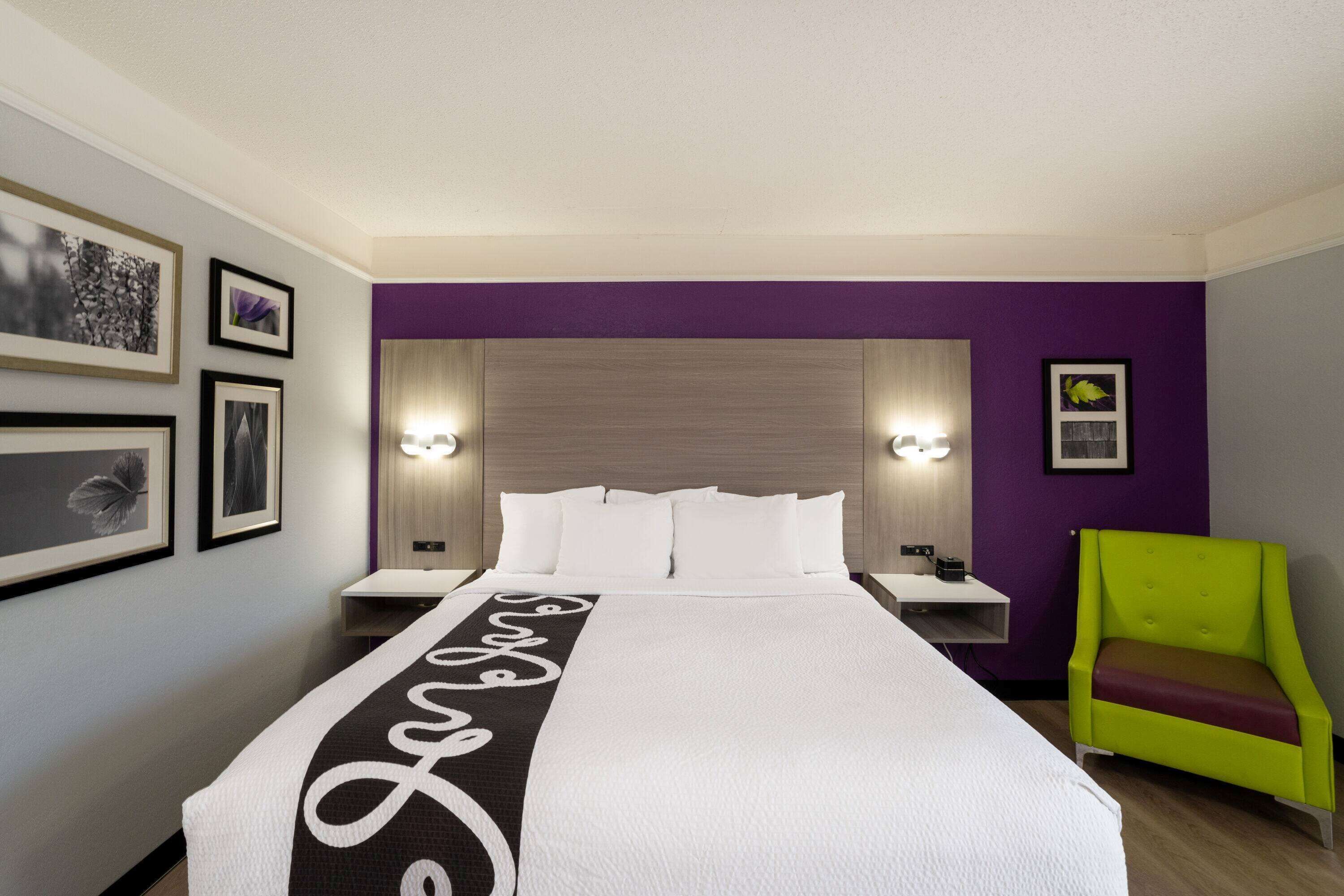A hotel room with a large bed, two bedside tables, a green armchair, and purple walls.