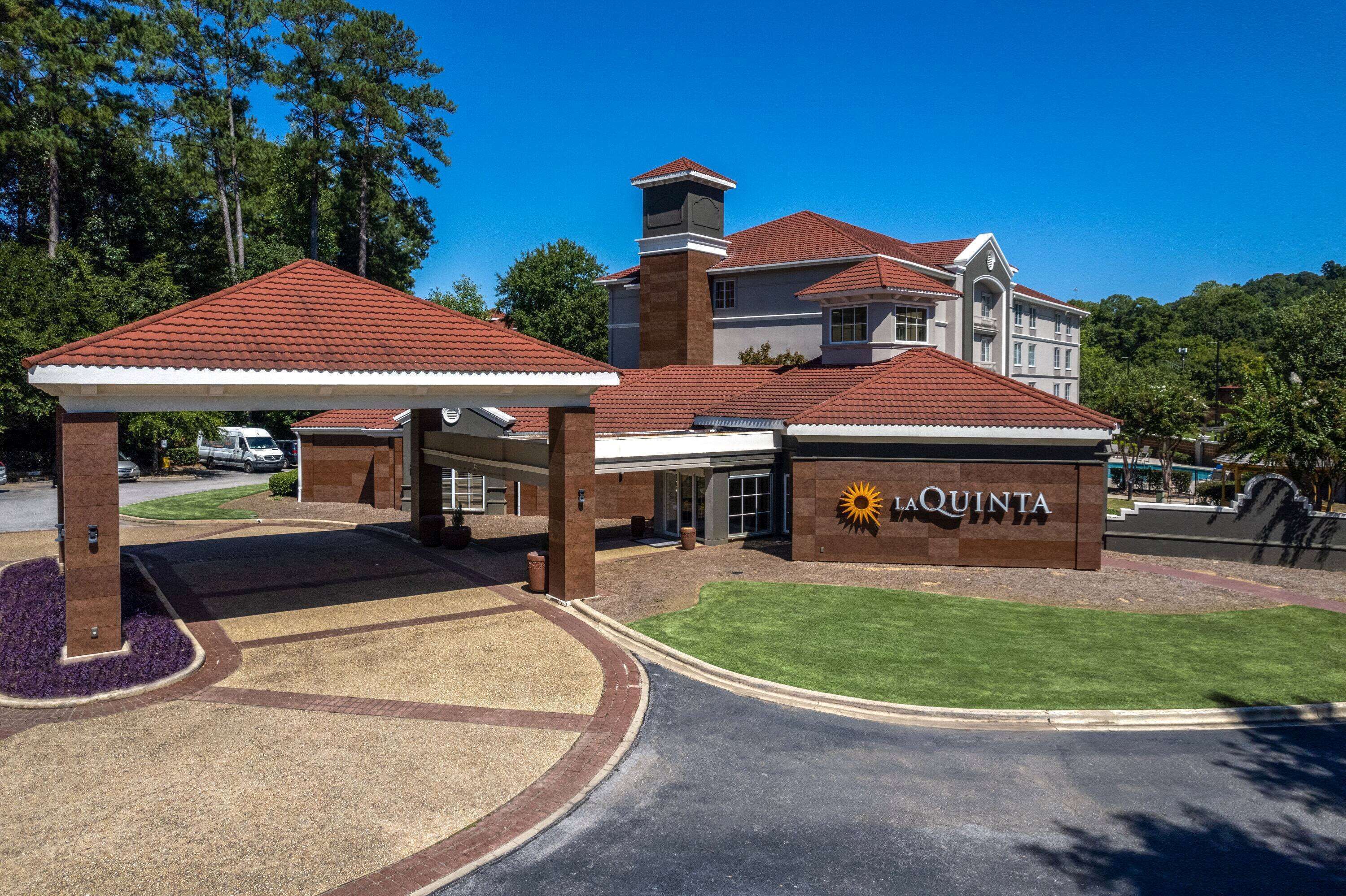 A hotel entrance with a covered parking area, a prominent sign reading "LaQuinta", and a well-maintained lawn.