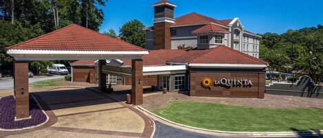 A hotel entrance with a covered parking area, a prominent sign reading "LaQuinta", and a well-maintained lawn.