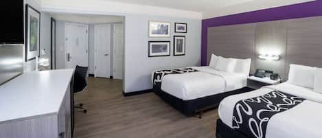 A hotel room with two beds, a desk, and a chair. There are framed pictures on the wall and a nightstand with a lamp.