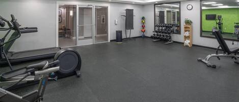 A gym with cardio equipment, weight racks, and a mirror.