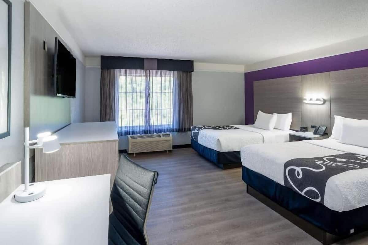 Habitación de hotel con dos camas, un escritorio, una silla, un televisor y una ventana con cortinas.