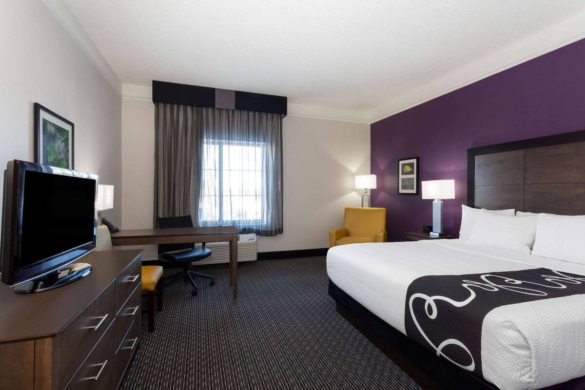 Ein Hotelzimmer mit Bett, Schreibtisch mit Fernseher, Stuhl, Lampe und einem Fenster mit Vorhängen.