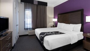 Una habitación de hotel con cama, televisión, escritorio y ventana con cortinas.