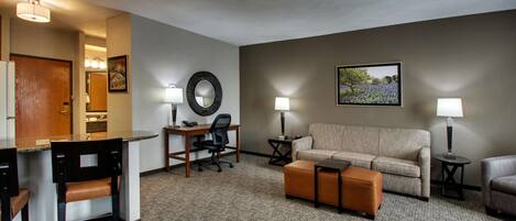 A hotel room with a kitchenette, a sofa, a desk with a chair, and a coffee table.