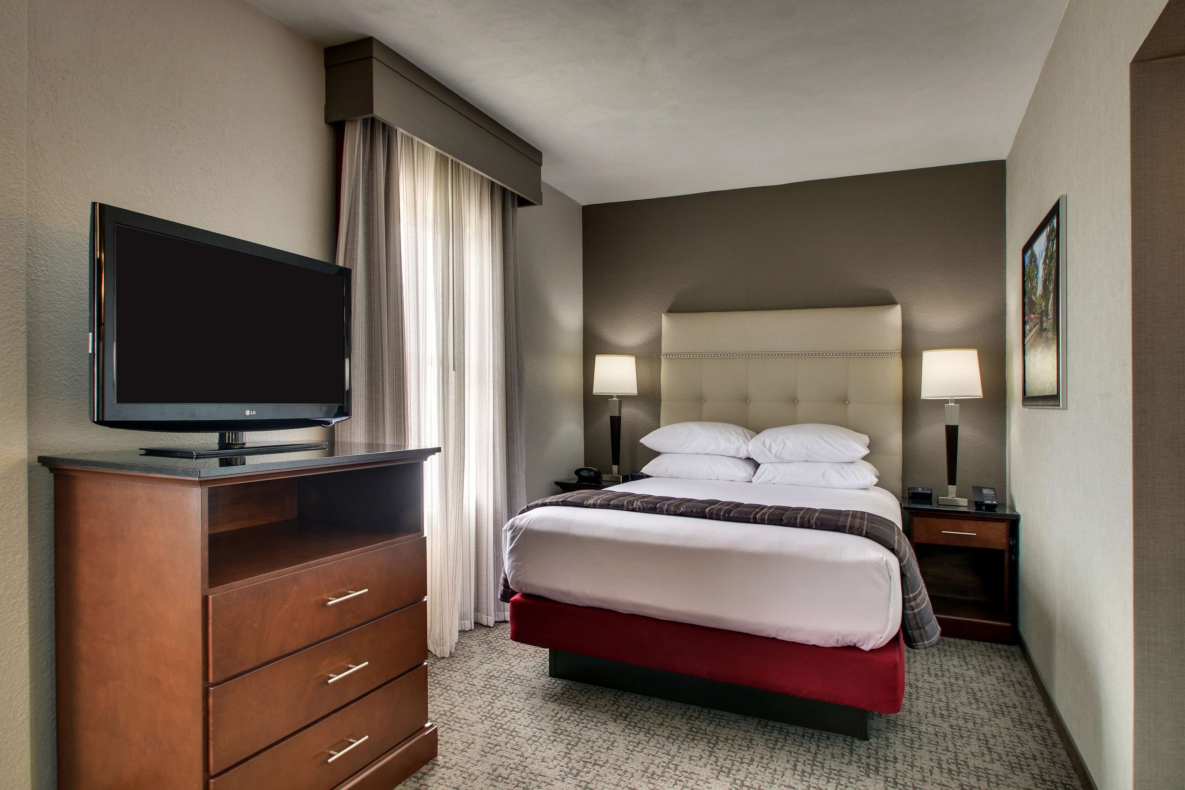 A hotel room with a bed, a TV on a wooden dresser, and two bedside lamps.