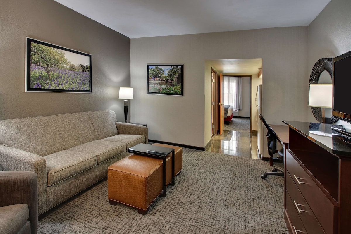A hotel room with a sofa, a coffee table, a TV, a desk, and a lamp.
