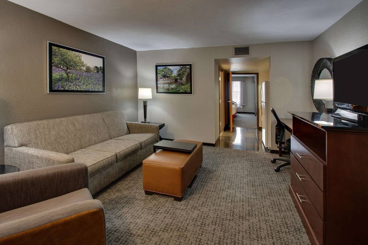 A hotel room with a sofa, a coffee table, a TV, a desk, and a dresser. There are two framed pictures on the wall.