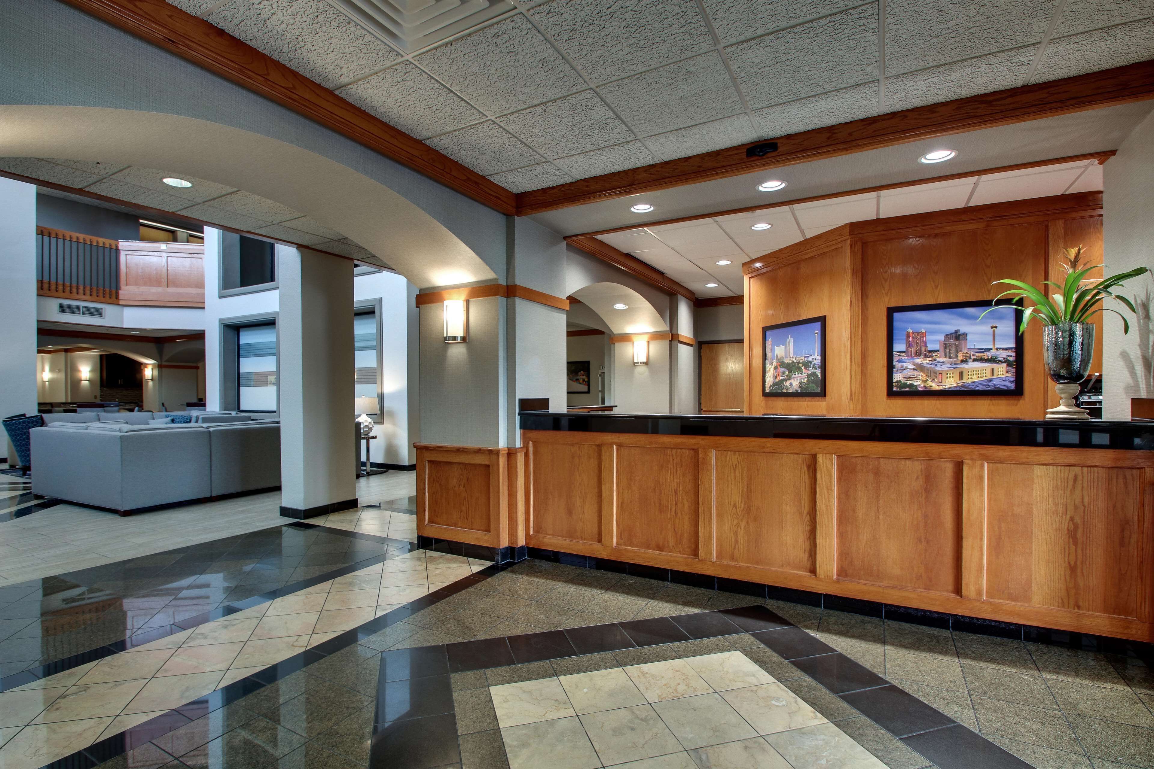 A hotel lobby with a reception desk, a large seating area, and a high ceiling with recessed lighting.