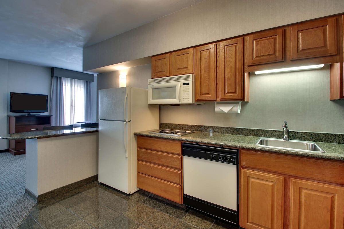 A compact kitchen with wooden cabinets, a microwave, a refrigerator, a dishwasher, and a built-in sink.