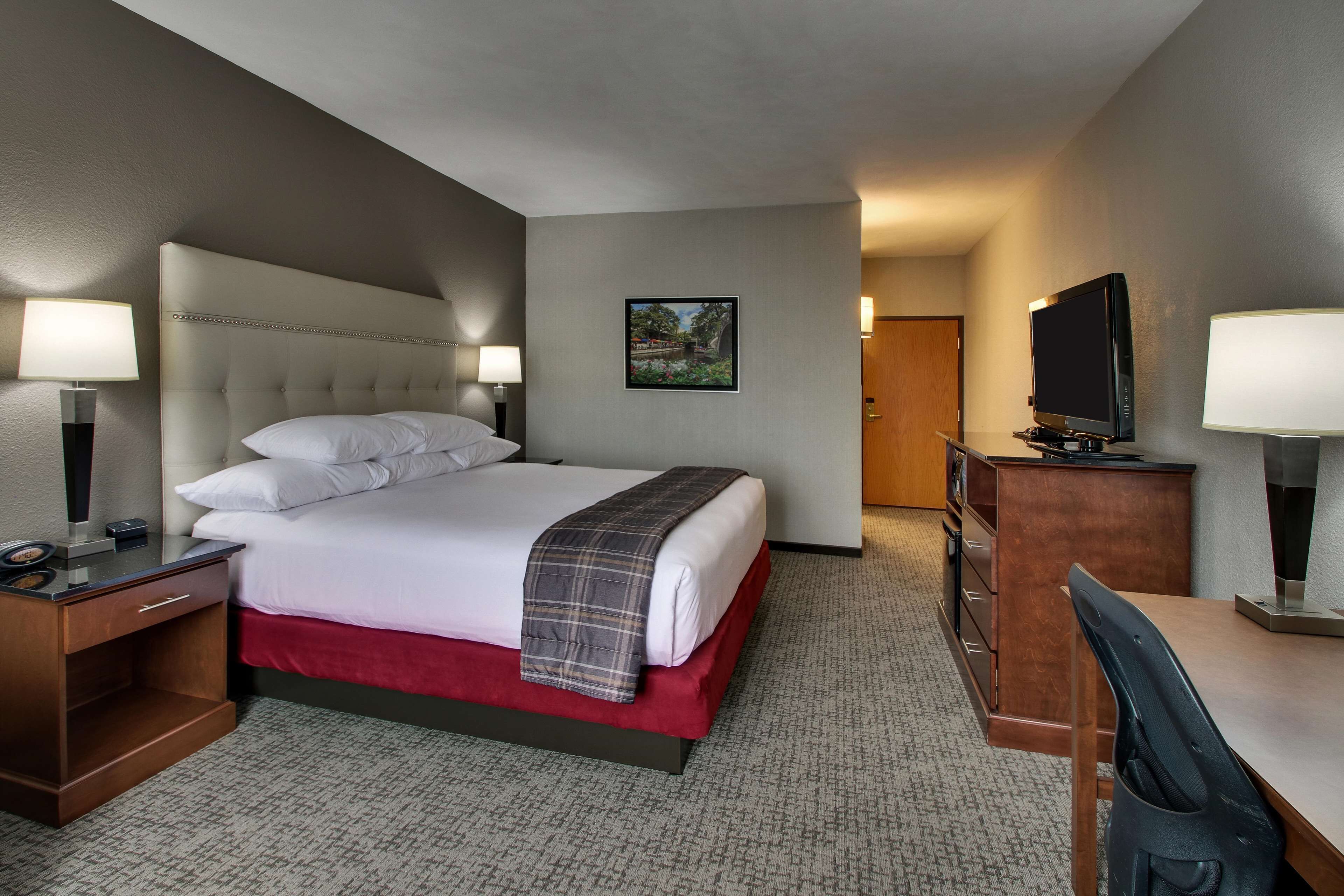 A hotel room with a bed, a desk, a chair, a TV, and a door.