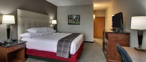 A hotel room with a bed, a desk, a chair, a TV, and a door.