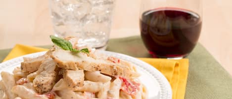 A plate of pasta with chicken and a glass of red wine.