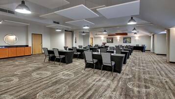 A conference room with multiple tables and chairs, a wooden cabinet, and a patterned carpet.