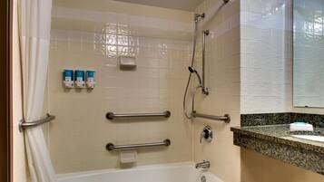 Un baño con bañera, barras de apoyo, cabezal de ducha y encimera con dispensador de jabón.