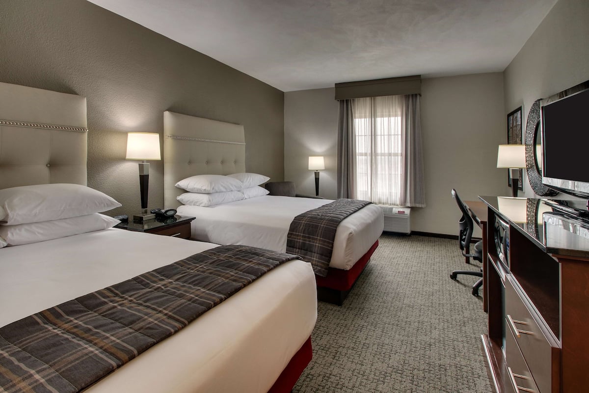 A hotel room with two beds, a desk, a television, and a window with curtains.