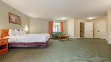 Una habitación de hotel con una cama, un sillón verde, una mesa de centro de madera y una puerta que da al baño.