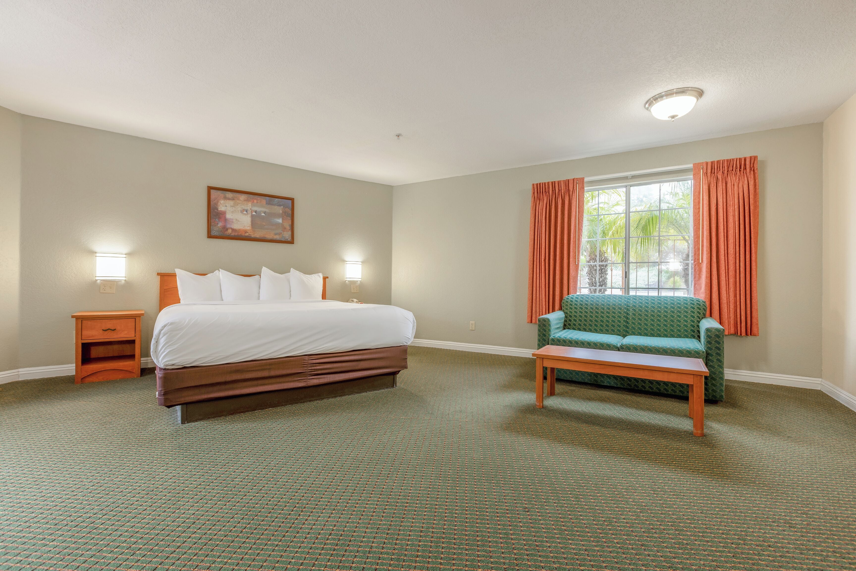 A hotel room with a large bed, a green sofa, a small table, and a window with curtains.