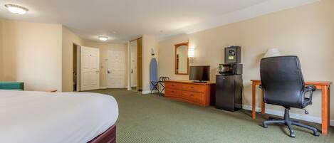 A hotel room with a bed, a dresser, a desk with a chair, a television, and a safe.