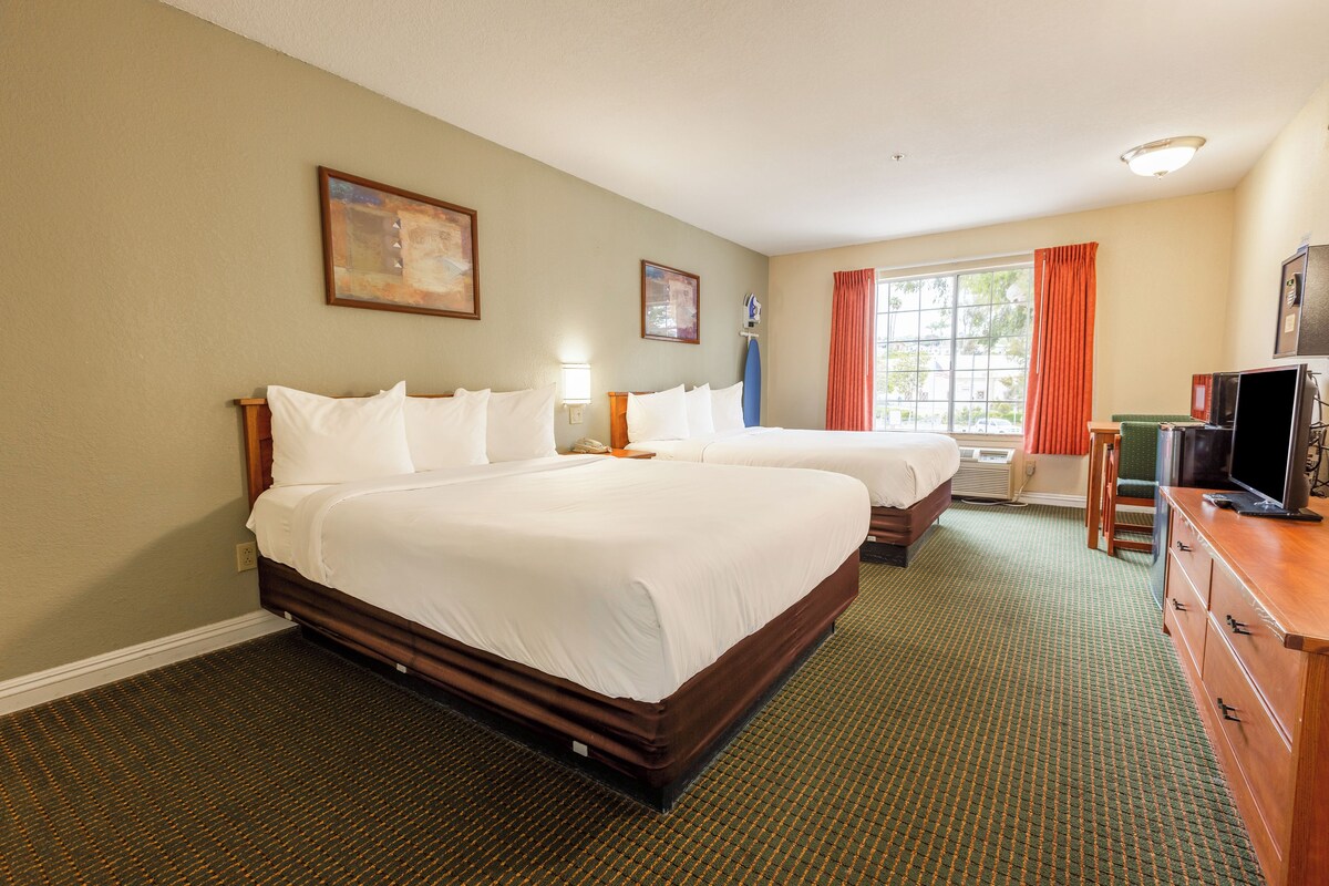 A hotel room with two beds, a television, a desk, and a window with curtains.