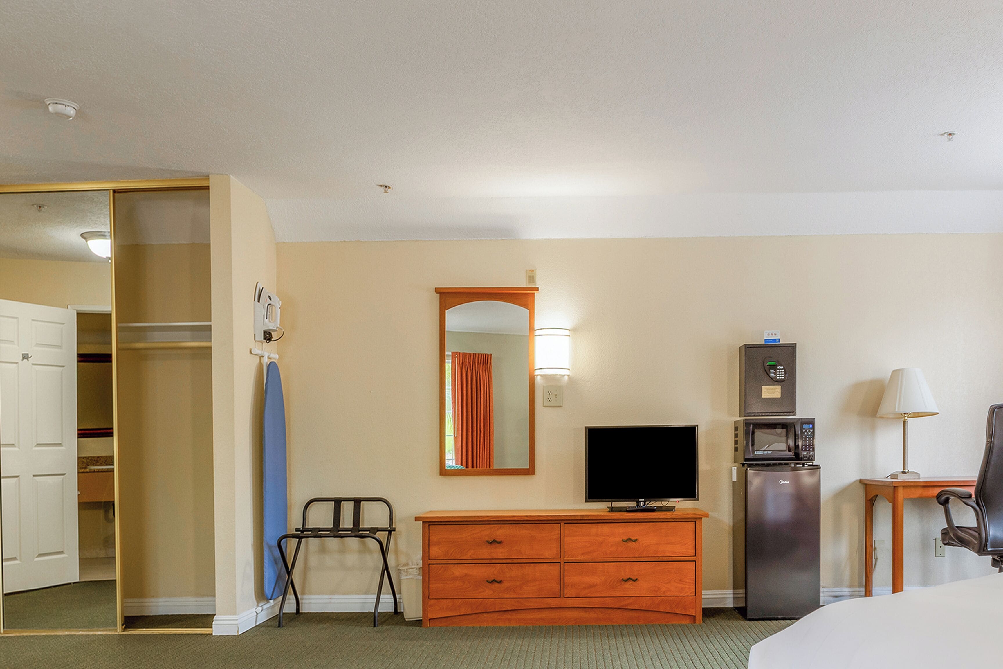Une chambre d’hôtel équipée d’une commode en bois, d’une télévision, d’un four à micro-ondes, d’un réfrigérateur, d’une chaise et d’un placard.