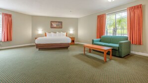 Quarto de hotel com cama, poltrona verde, mesa de madeira, mesa de cabeceira e janela com cortinas.
