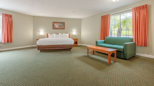 A hotel room with a bed, a green armchair, a wooden table, a nightstand, and a window with curtains. - Hotel Avenida, San Clemente Beach (San Clemente)