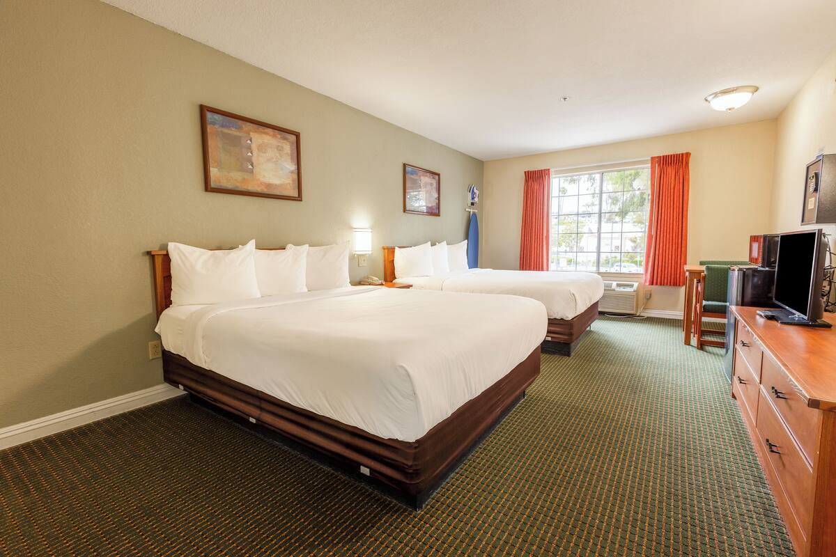 A hotel room with two beds, a television, a desk, and a window with curtains.
