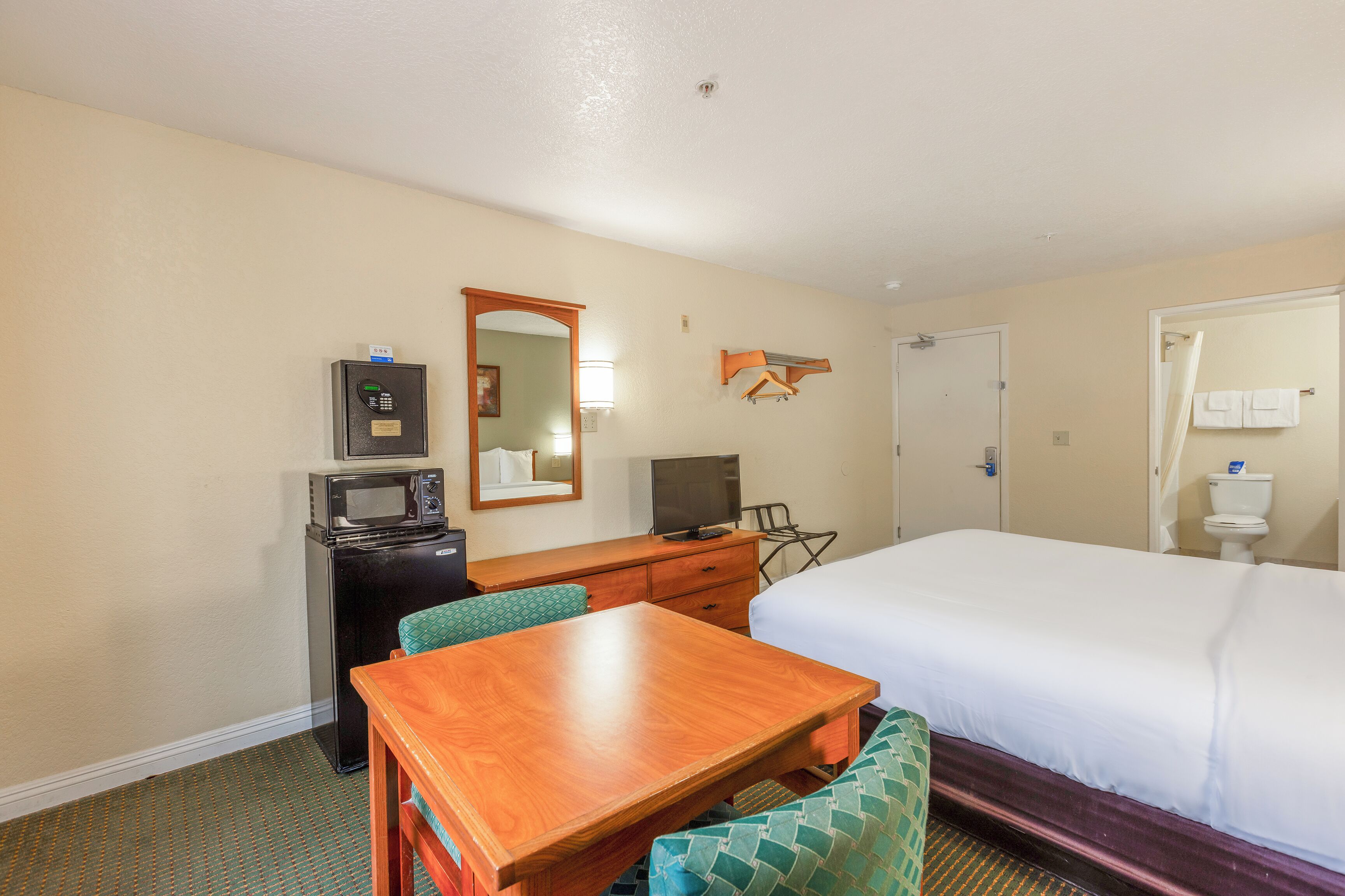 Camera d'albergo con un letto, una scrivania con computer e televisione, un piccolo frigorifero, uno specchio e un bagno con servizi igienici e lavandino.