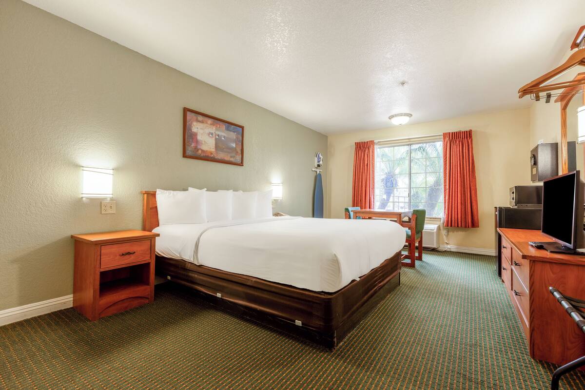 A hotel room with a bed, bedside table, desk, television, and a window with curtains.