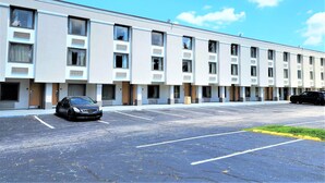A row of single-story motel rooms with individual doorways, a parking lot, and a clear blue sky. - Motel 6 Catonsville, MD – Baltimore West (Catonsville)
