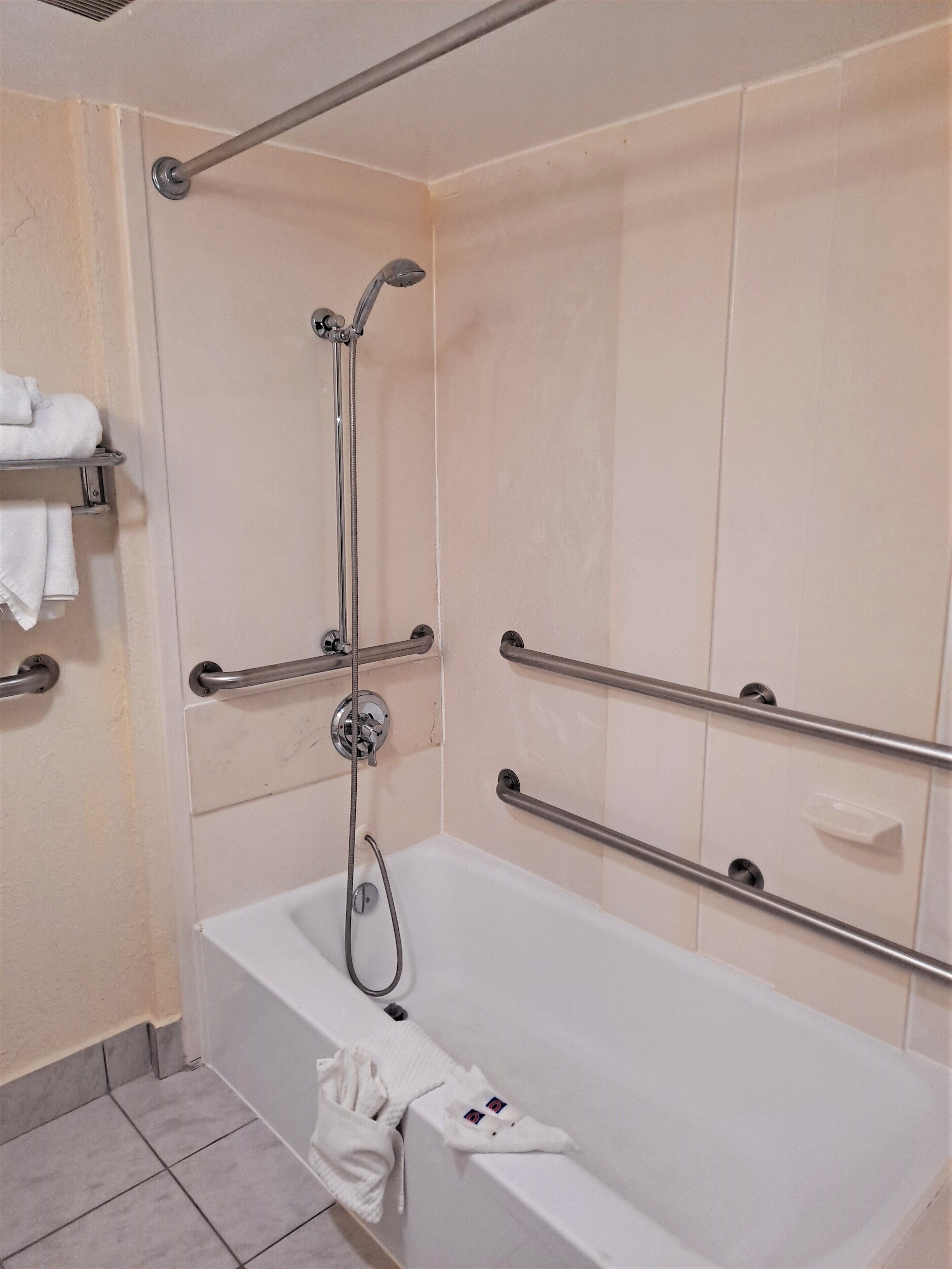 Une salle de bain avec une baignoire blanche, des barres d’appui, une pomme de douche et un porte-serviettes.