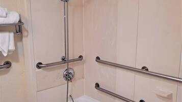 Un baño con una bañera blanca, barras de apoyo, ducha y un perchero para toallas.