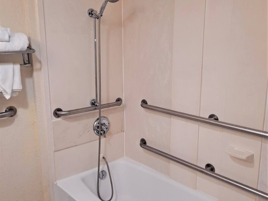 Un baño con una bañera blanca, barras de apoyo, ducha y un perchero para toallas.