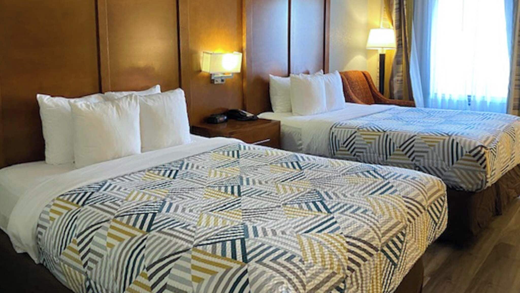 A hotel room with two beds, each with a patterned bedspread, bedside lamps, and a nightstand with a phone.