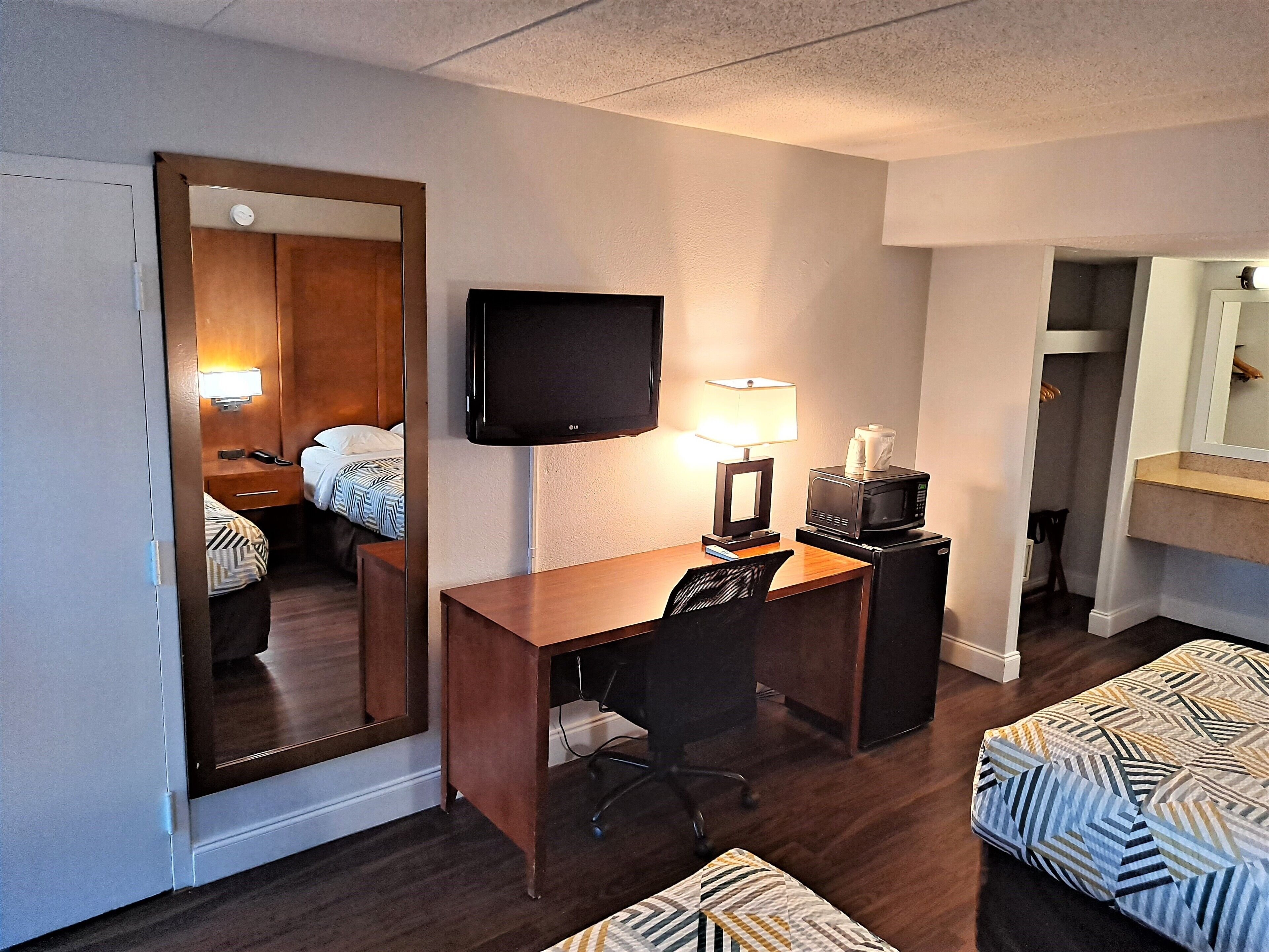 A hotel room with a wooden desk, a television, a lamp, a microwave, a chair, and two beds with patterned bedding.