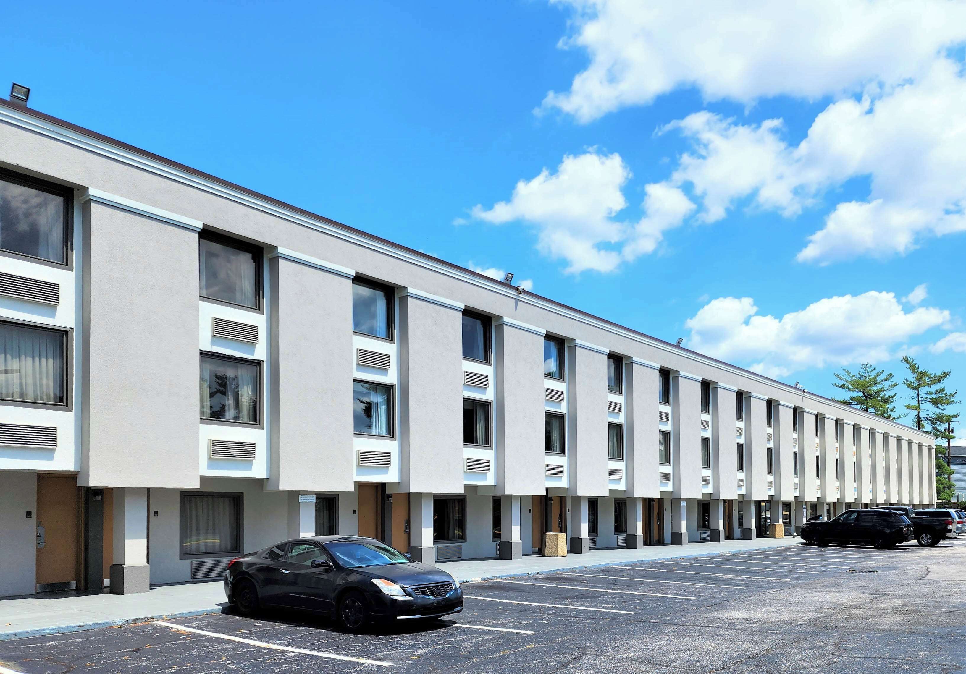 Un hôtel moderne avec une série de chambres, un parking et un ciel d’un bleu éclatant.