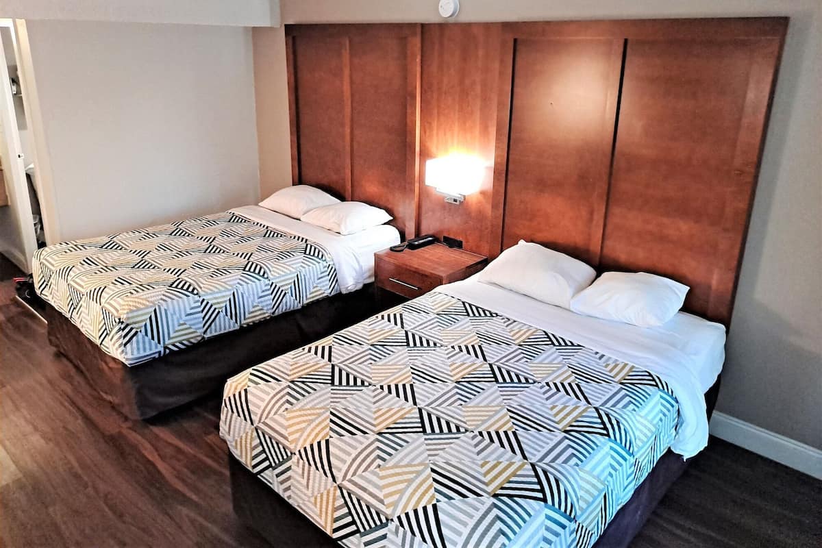 Ein Hotelzimmer mit zwei Betten, jeweils mit einem gemusterten Überwurf, einem Holzkopfende und einem Nachttisch mit einer Lampe.