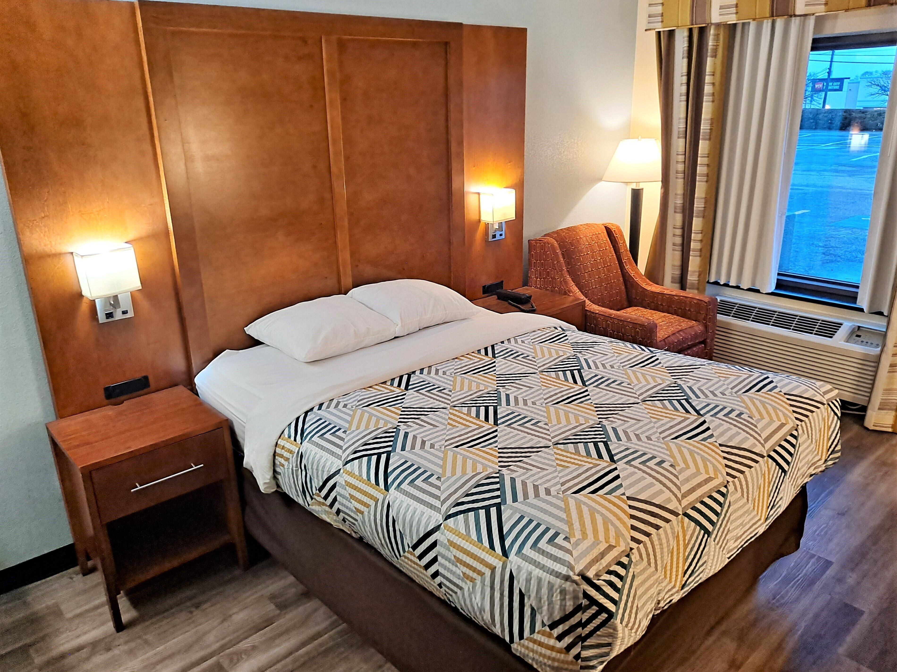 A hotel room with a large bed, a nightstand, a chair, and a window with curtains.