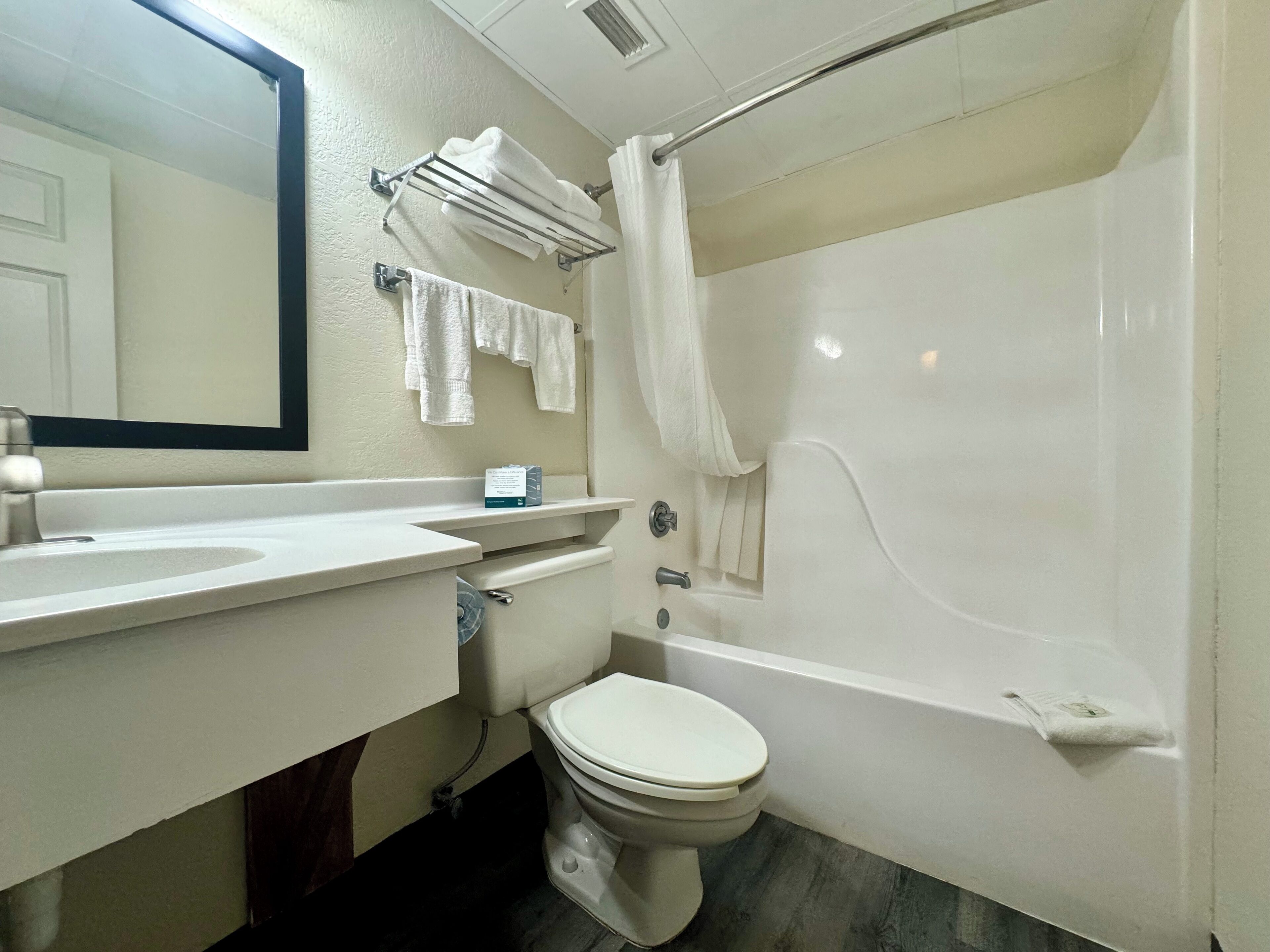Un baño con inodoro, lavabo y bañera. Hay un perchero con toallas y una cortina de ducha.